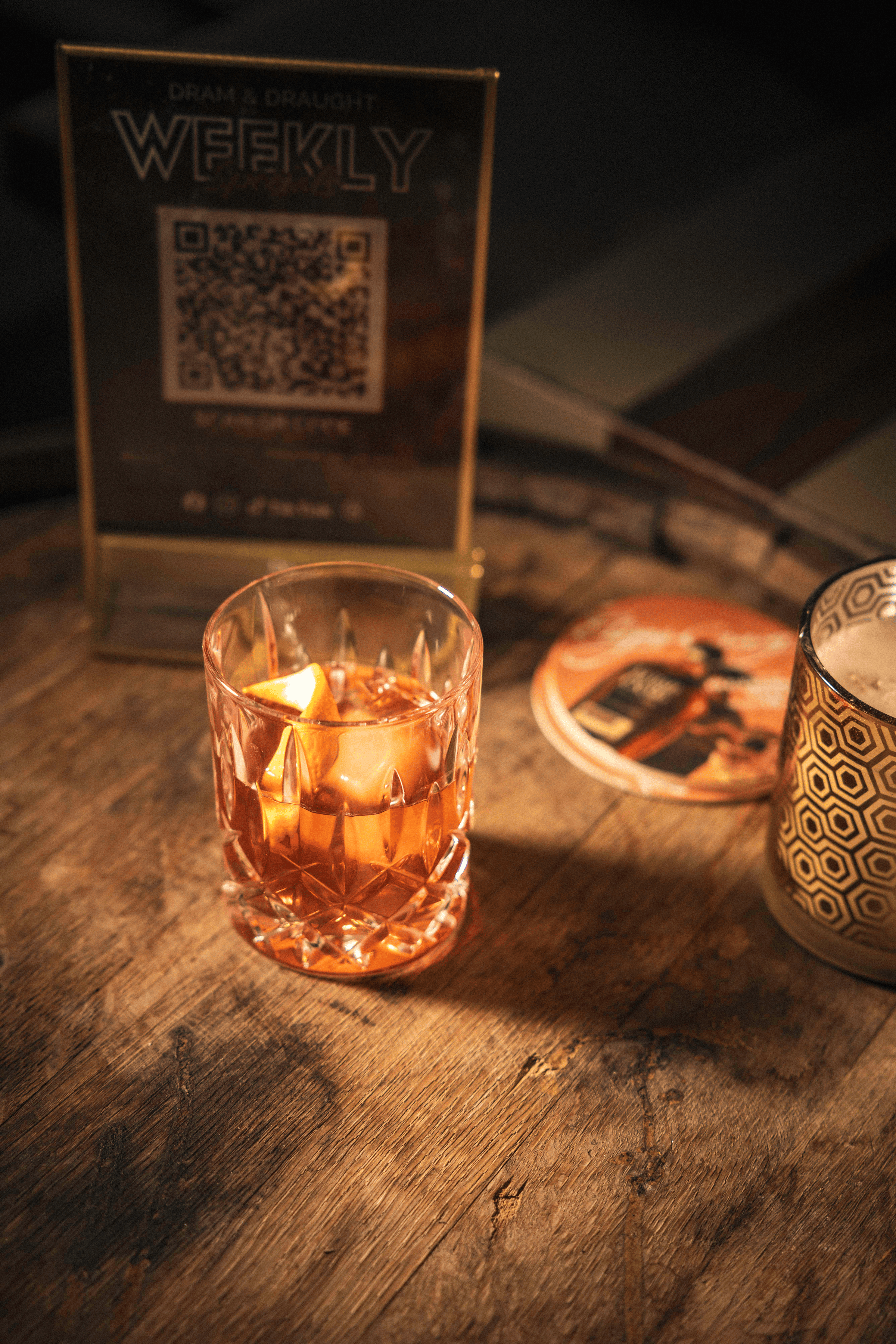 A beautifully crafted cocktail sits in a crystal glass, casting warm amber reflections on a rustic wooden table.