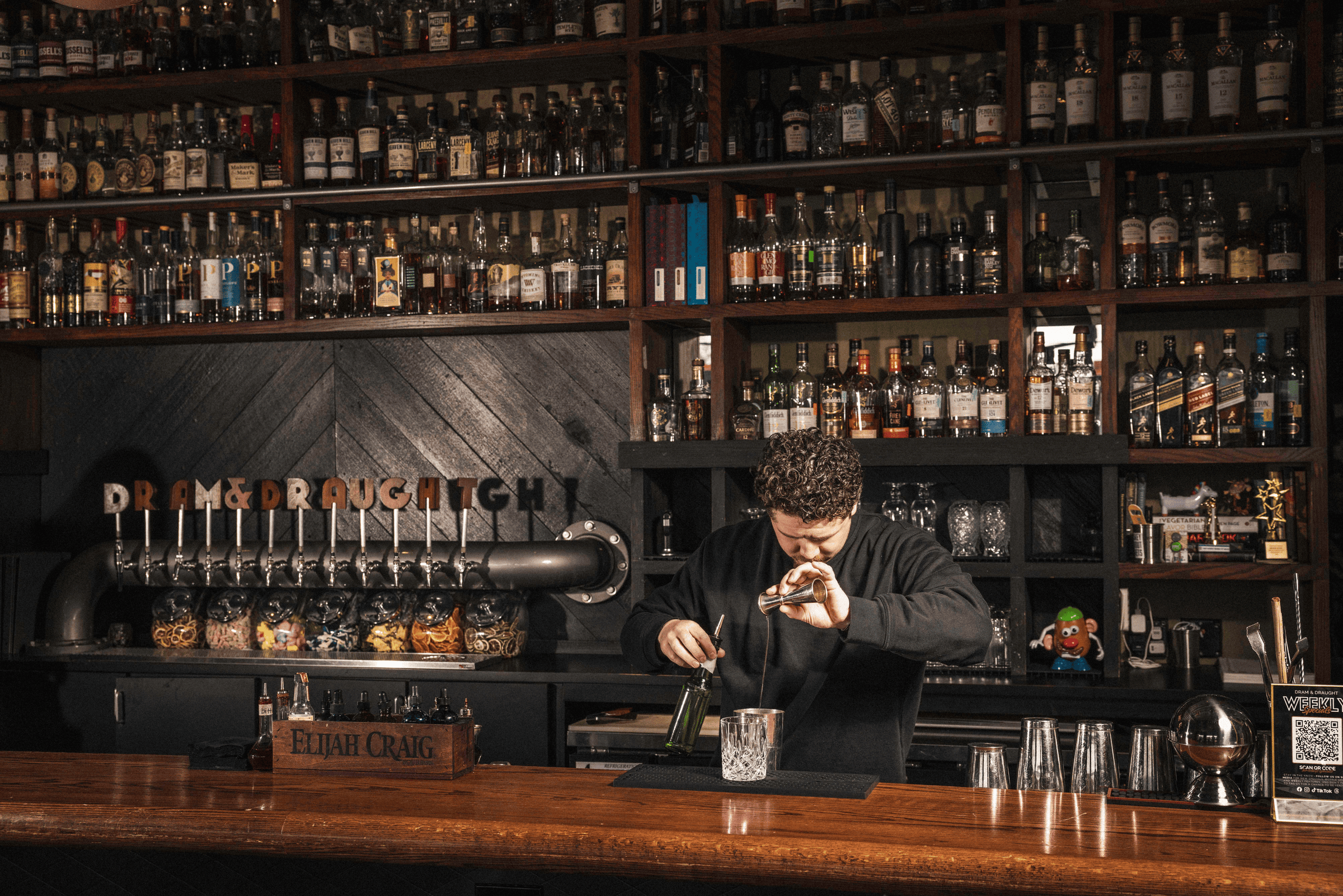 A bartender skillfully mixes a cocktail amid a backdrop of shelves lined with elegantly arranged liquor bottles.