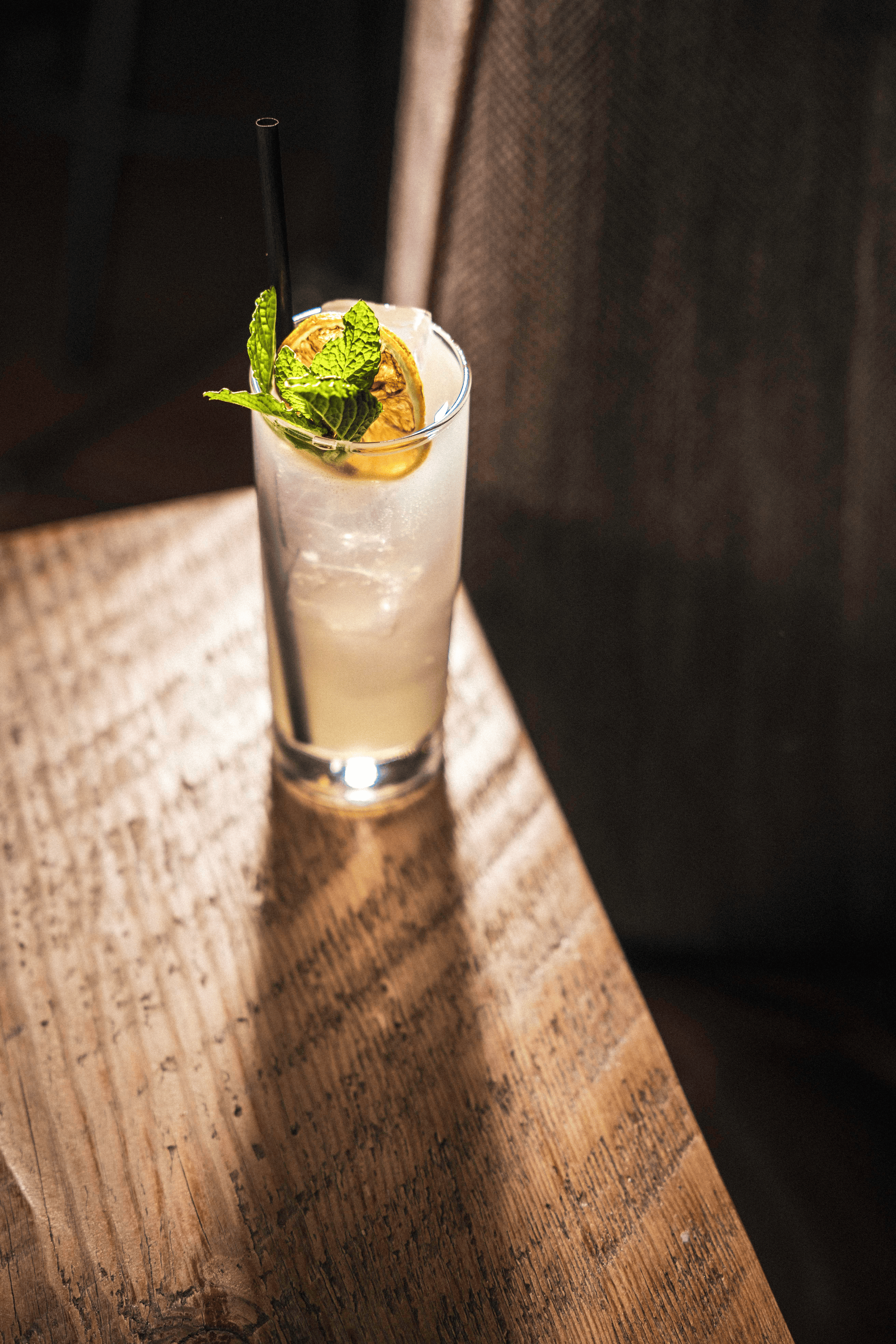 A refreshing cocktail garnished with mint and a dried lemon slice rests on a rustic wooden table, bathed in warm light.